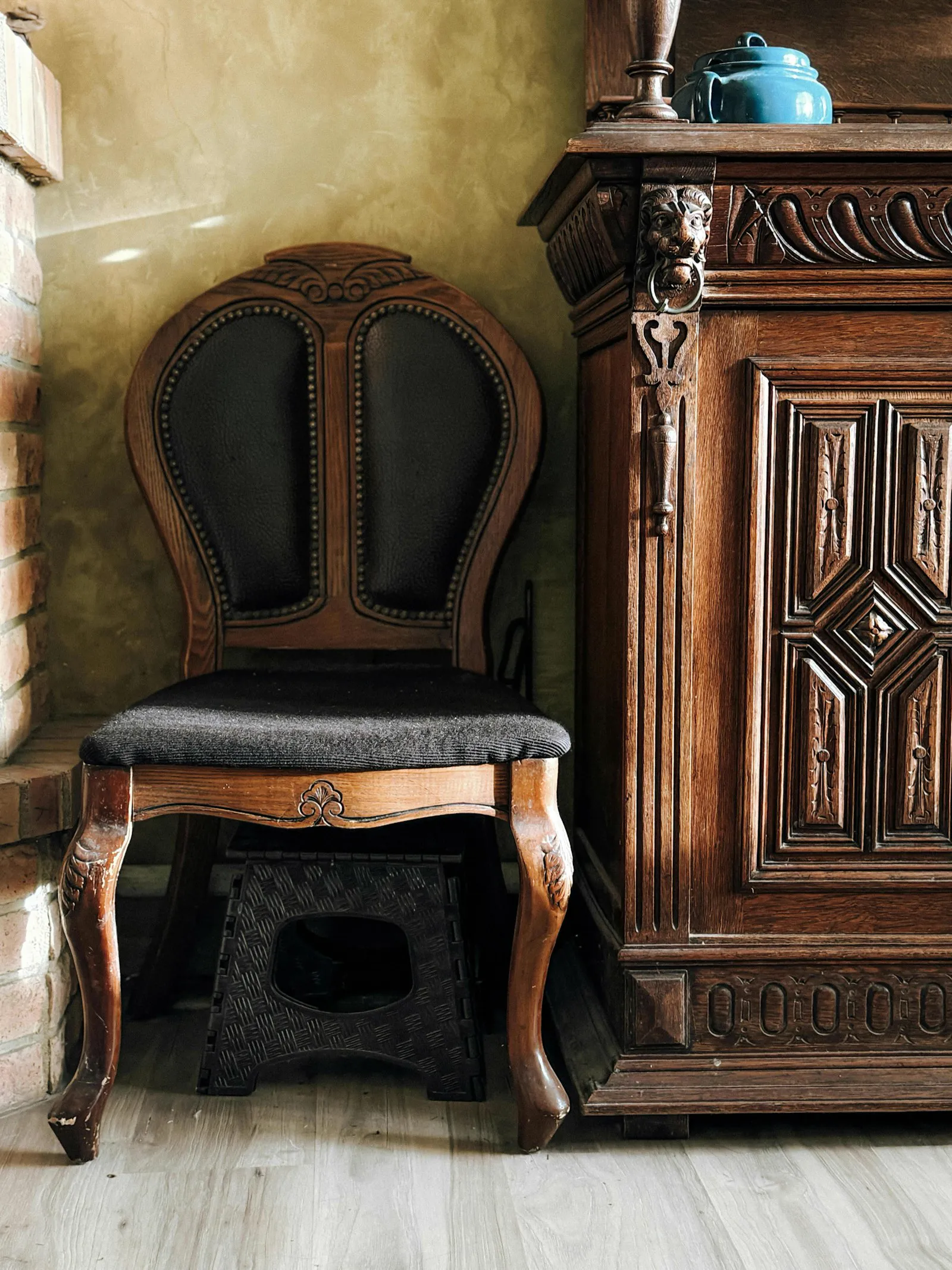 Antique carved wooden cabinet beside an upholstered carved chair
